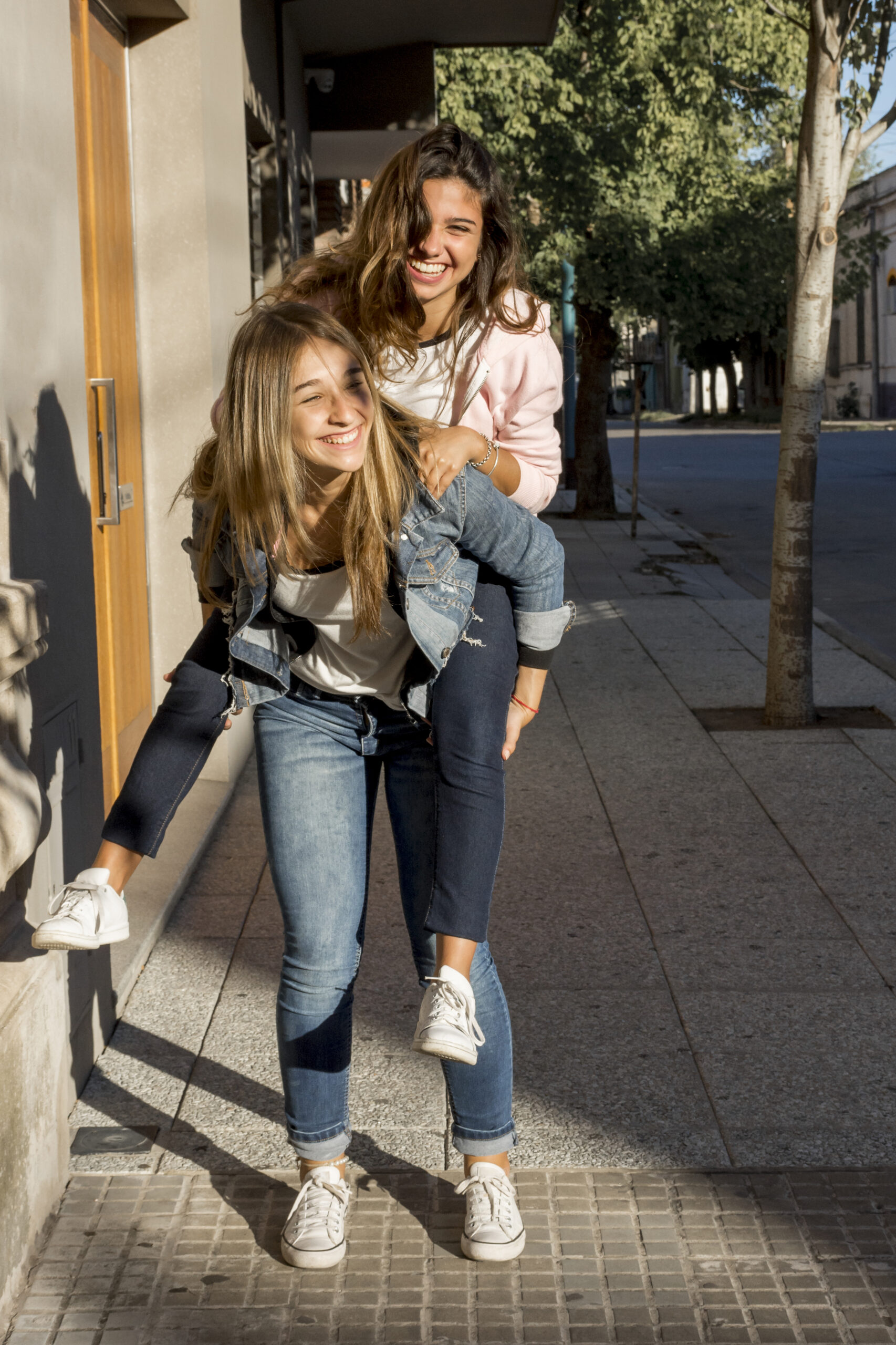 gorgeous-young-girl-giving-piggyback-her-female-friend-sidewalk