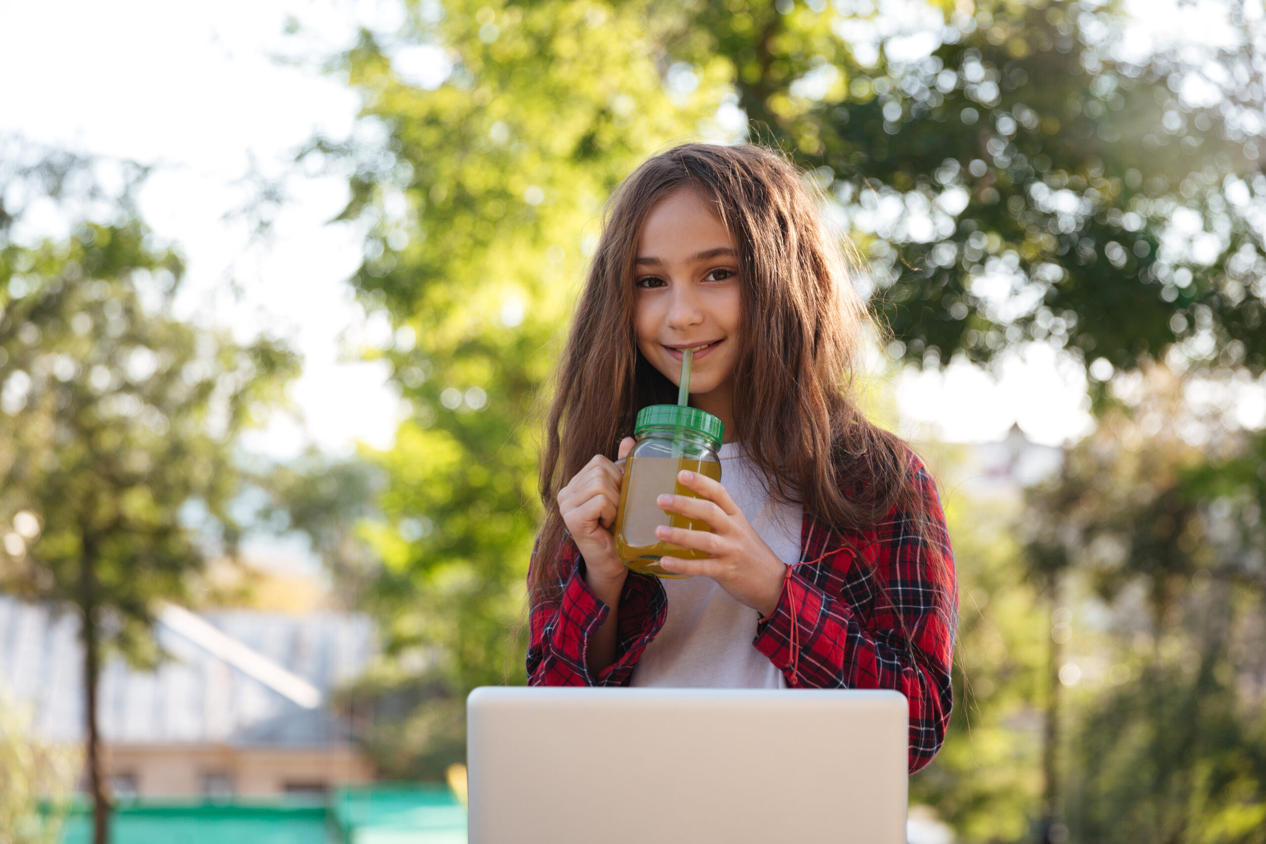 Smiling young brunette woman sitting in park with laptop computer